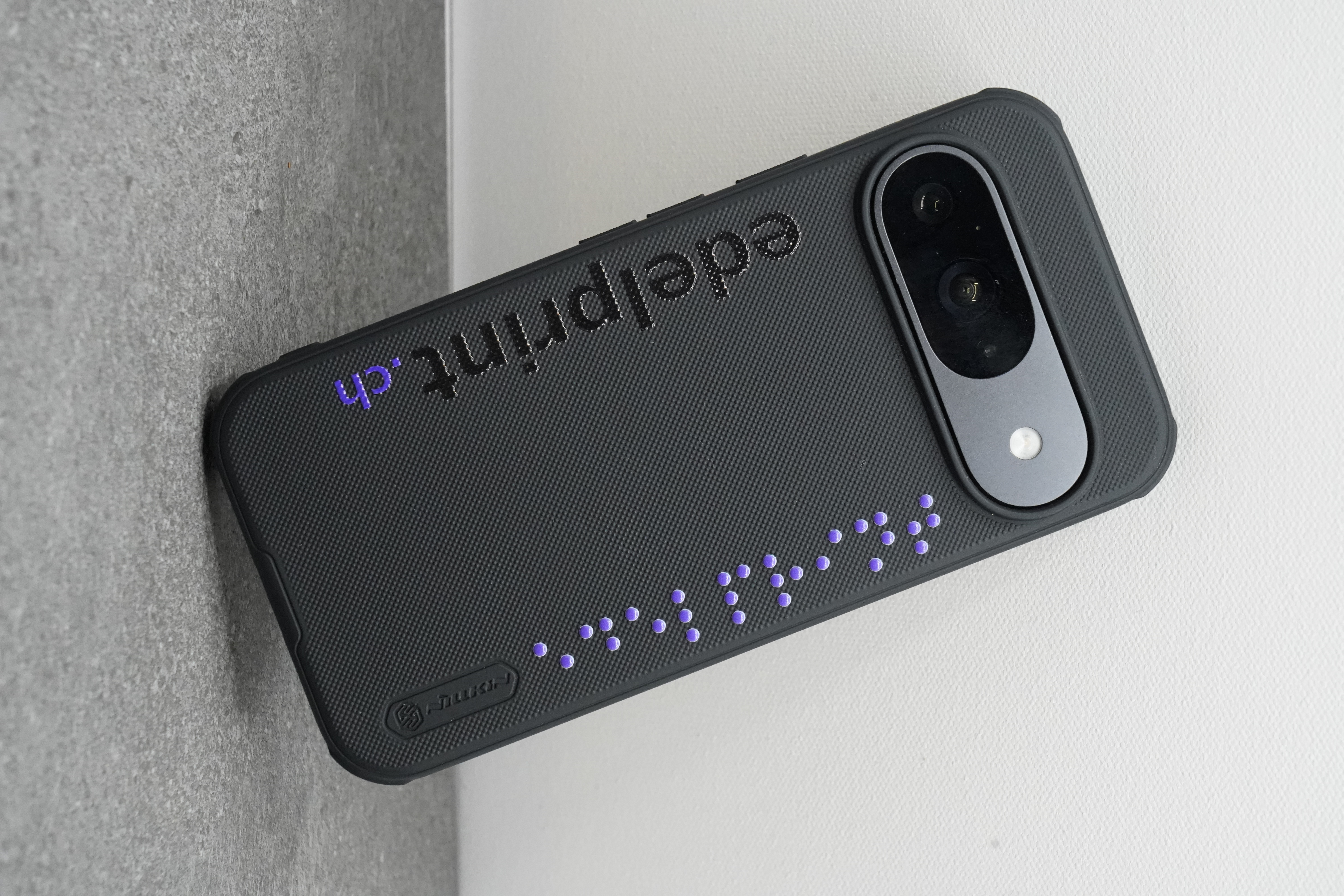 Handyhülle in Schwarz mit erhabenen lila Braille-Punkten und edelprint.ch-Schriftzug in Weissunterdruck — Braille als Design-Element auf Alltagsobjekt