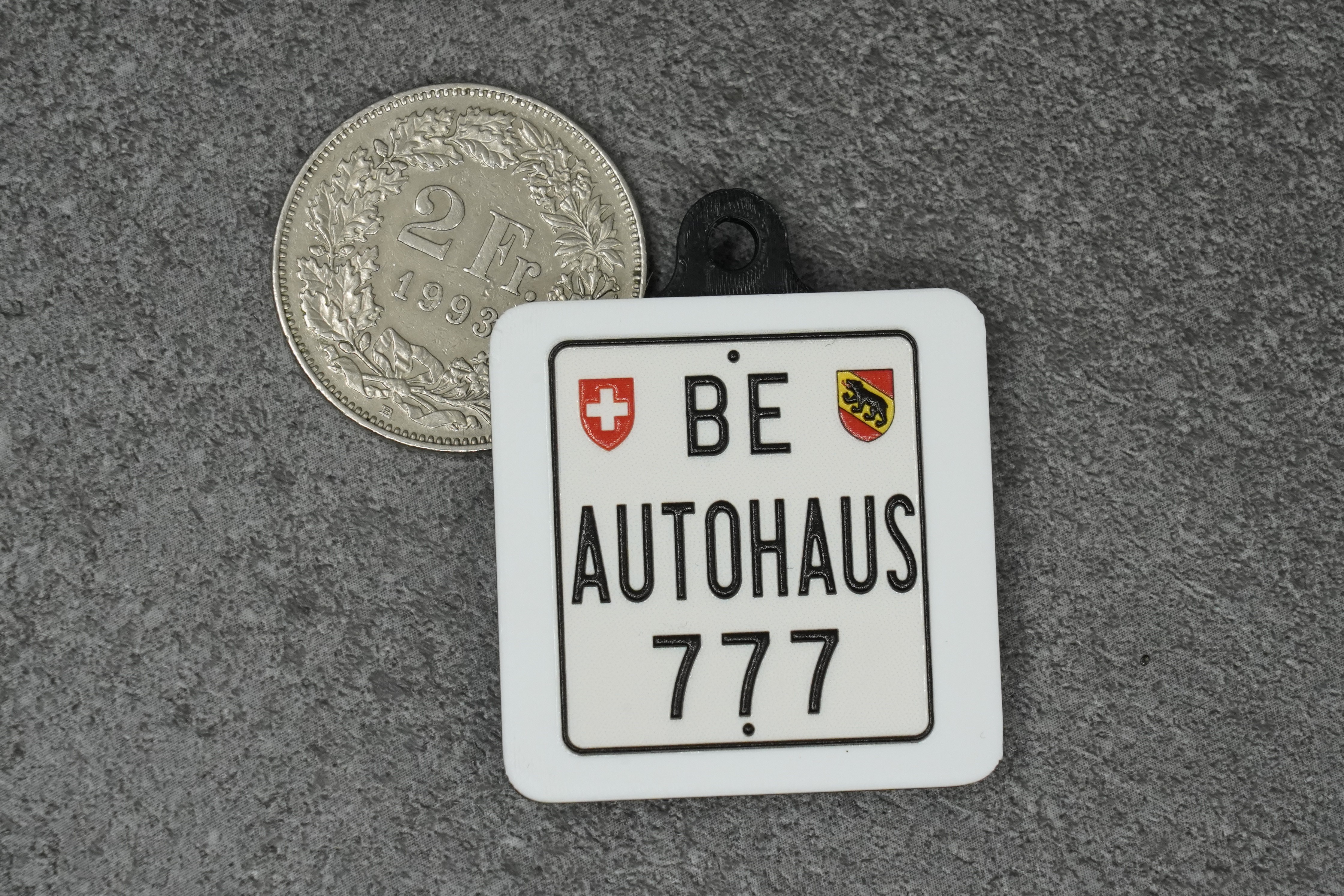 Miniatur-Autohaus-Kennzeichen «BE Autohaus 777» in Vollfarbe, im Grössenvergleich mit einer 2-Franken-Münze